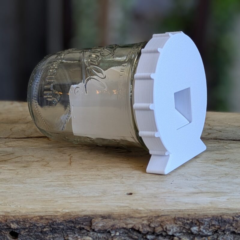 Mason jar mousetrap with a black CatchCap lid resting horizontally.